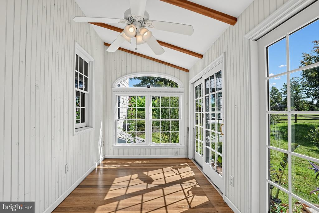 Unfurnished sunroom with vaulted wood-beam ceiling, hardwood floors, and large windows overlooking a green lawn.