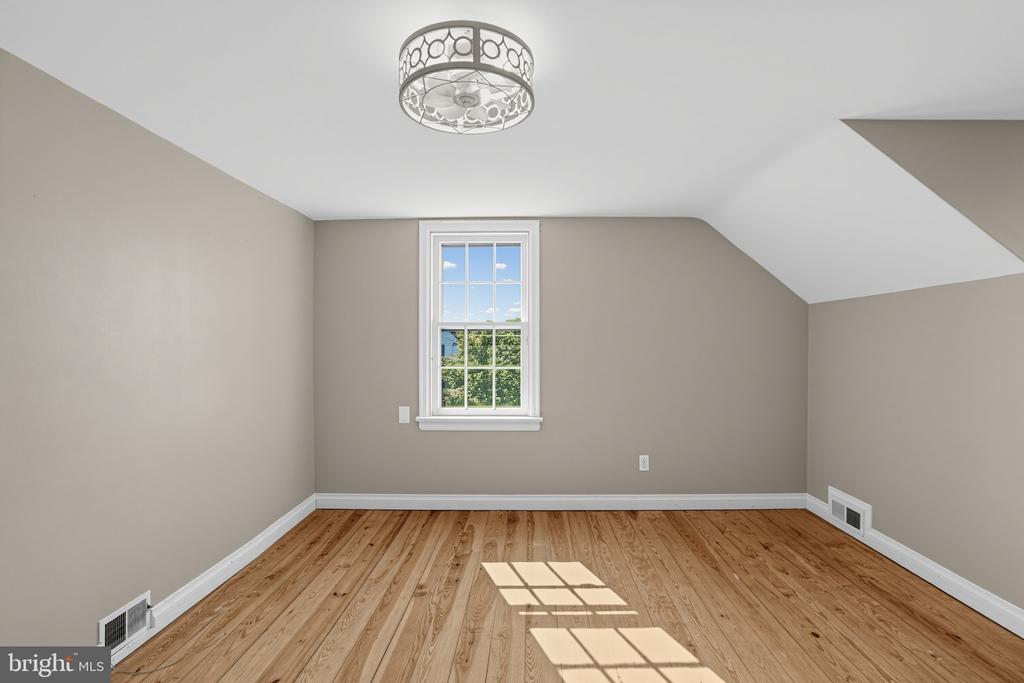 Empty upstairs room with sloped ceilings, wood flooring, and a window overlooking greenery.