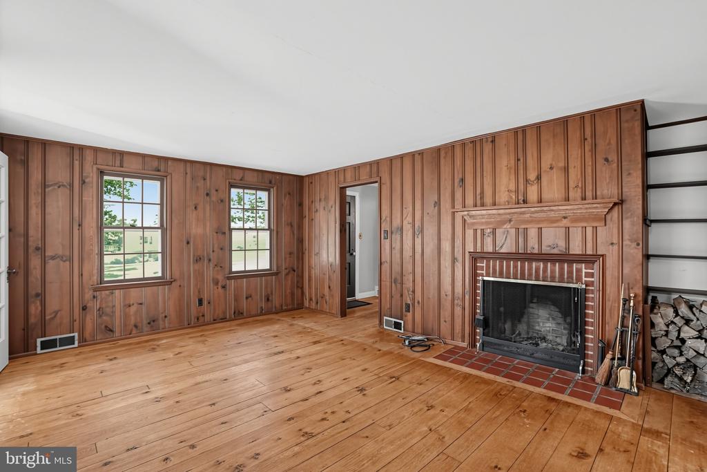 Unfurnished living room with knotty pine walls, hardwood floors, and a fireplace.