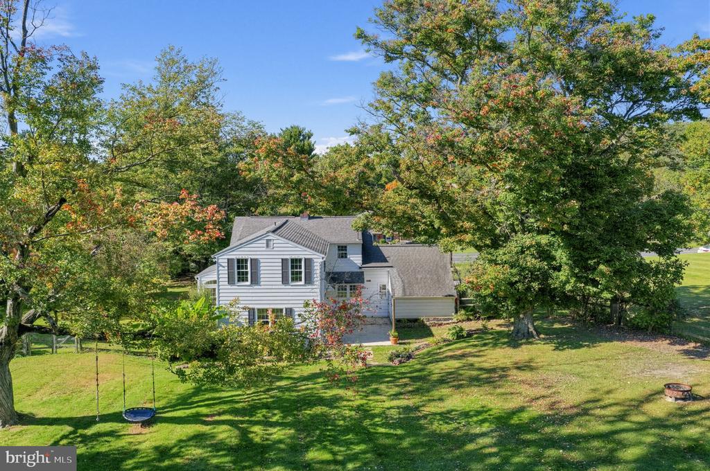 White-sided two-story house among mature trees, with a lawn swing and small garden.