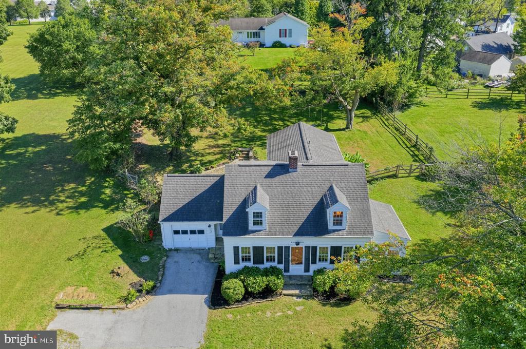 Aerial view of a white home with gray roof, attached garage, and fenced green yard.