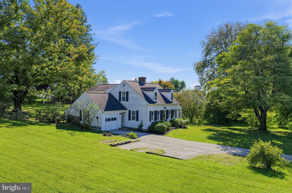White two-story house with dark shutters, a garage, and a wide lawn framed by mature trees.