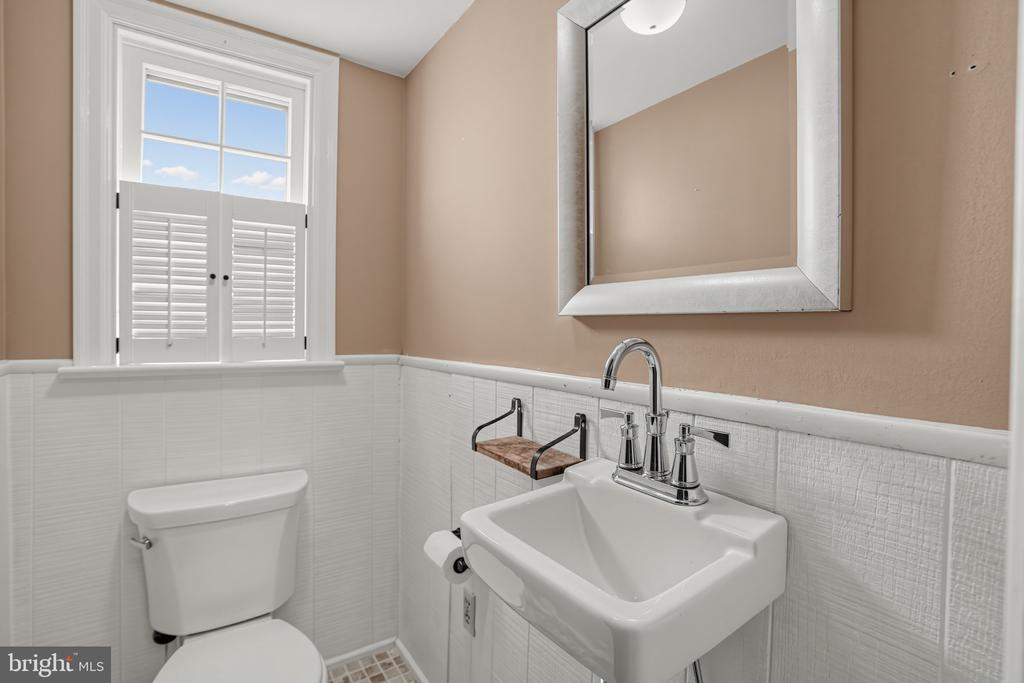 Bathroom with a white pedestal sink, large mirror, and shuttered window above the toilet.