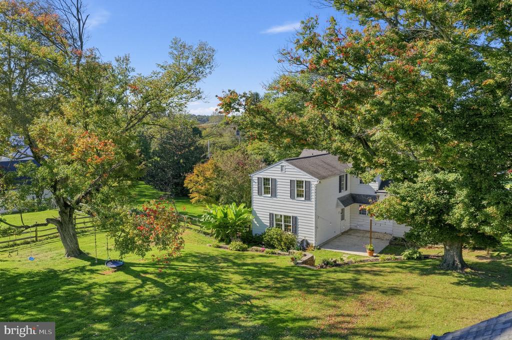 White two-story house among mature trees in a spacious, landscaped yard.