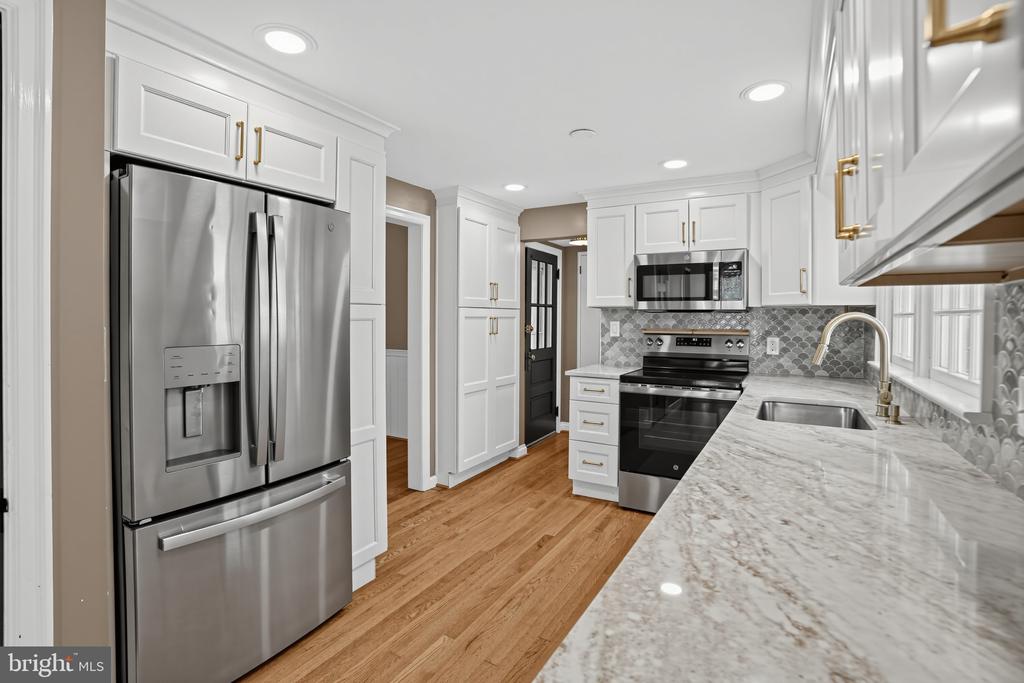 Renovated kitchen with white cabinets, stainless steel appliances, patterned backsplash, and hardwood floors.