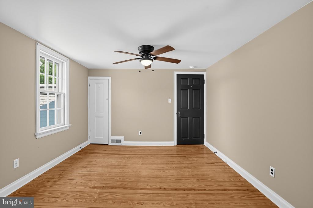 Vacant room with hardwood floors, a ceiling fan, one window, and a black entry door.