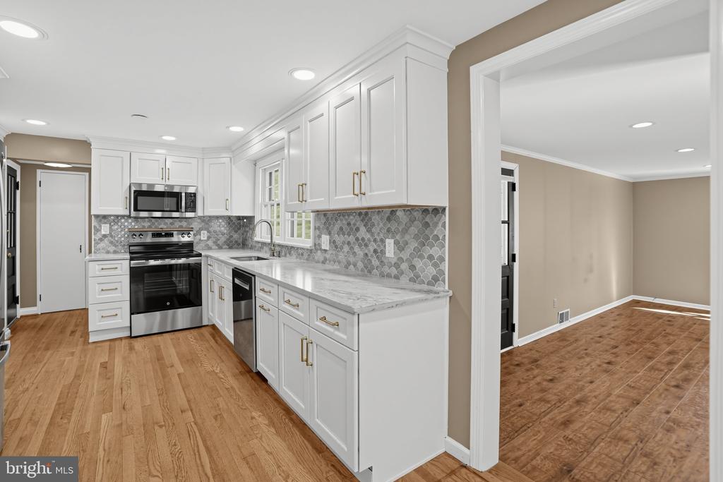 Kitchen with white cabinets, gray patterned tile backsplash, stainless steel appliances, and hardwood floors.