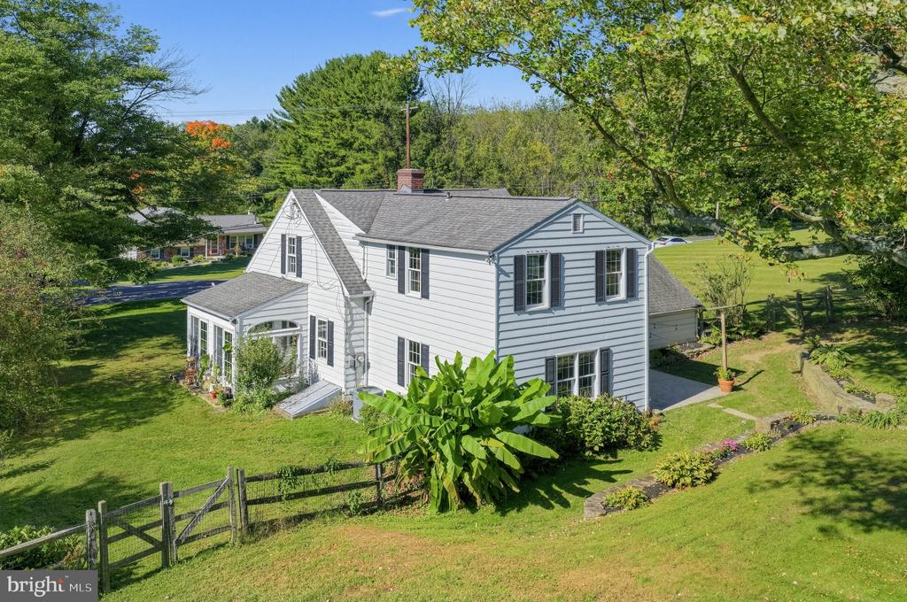 White two-story house with a sunroom, fenced lawn, and mature trees.