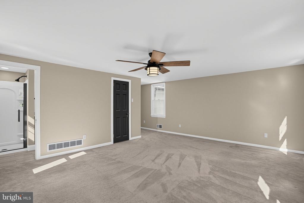 Empty carpeted bedroom with beige walls, a black door, and a ceiling fan.