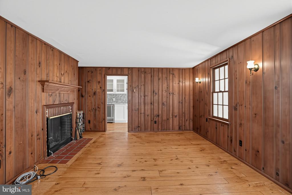 Vacant wood-paneled living room with a brick fireplace and doorway to the kitchen.