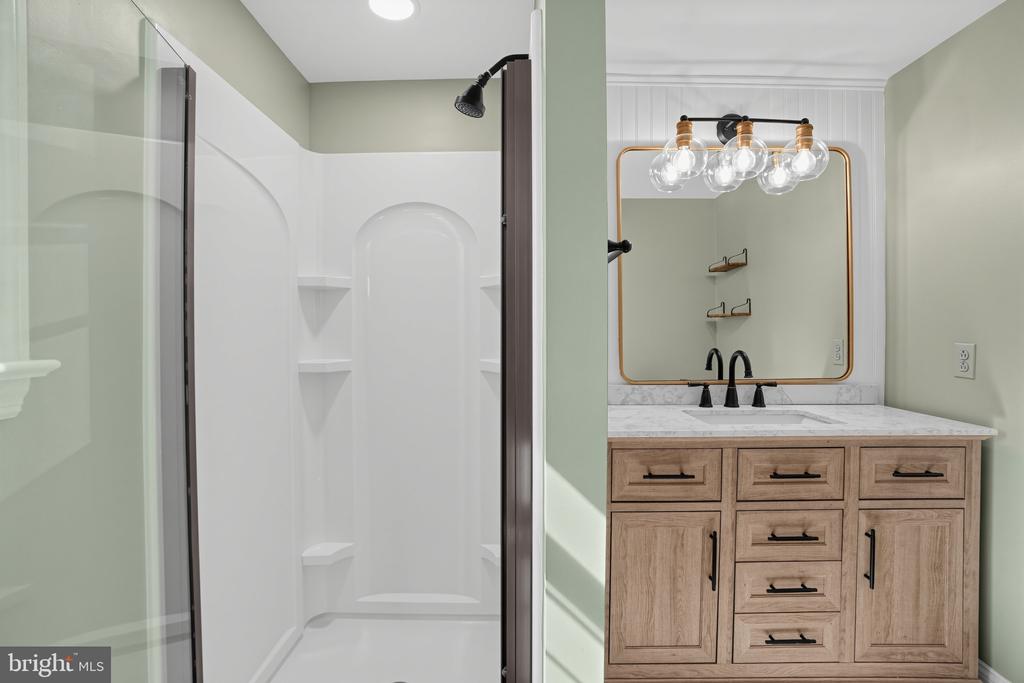 Bathroom with a white shower enclosure and light wood vanity topped with marble.