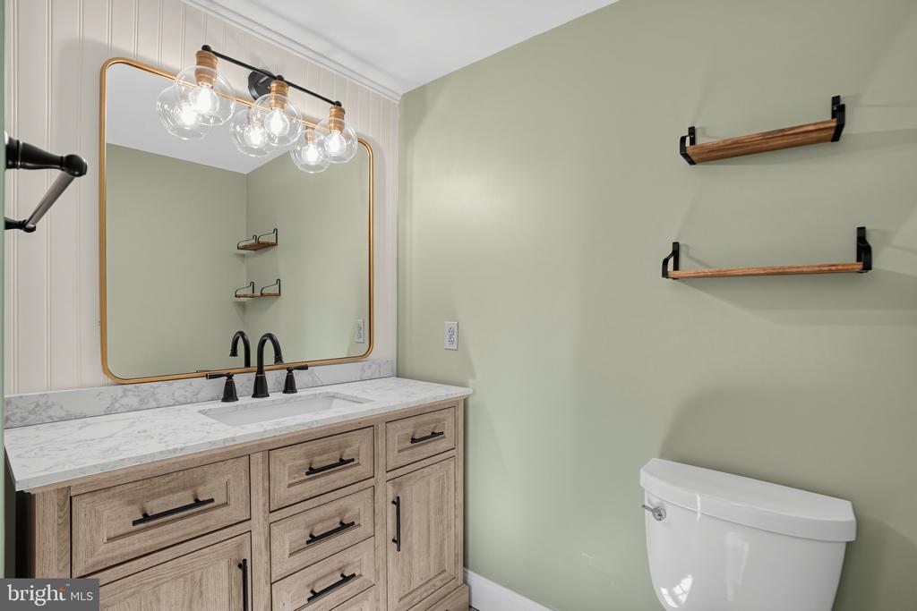 Bathroom vanity with a gold-framed mirror, marble-look counter, floating shelves, and toilet.