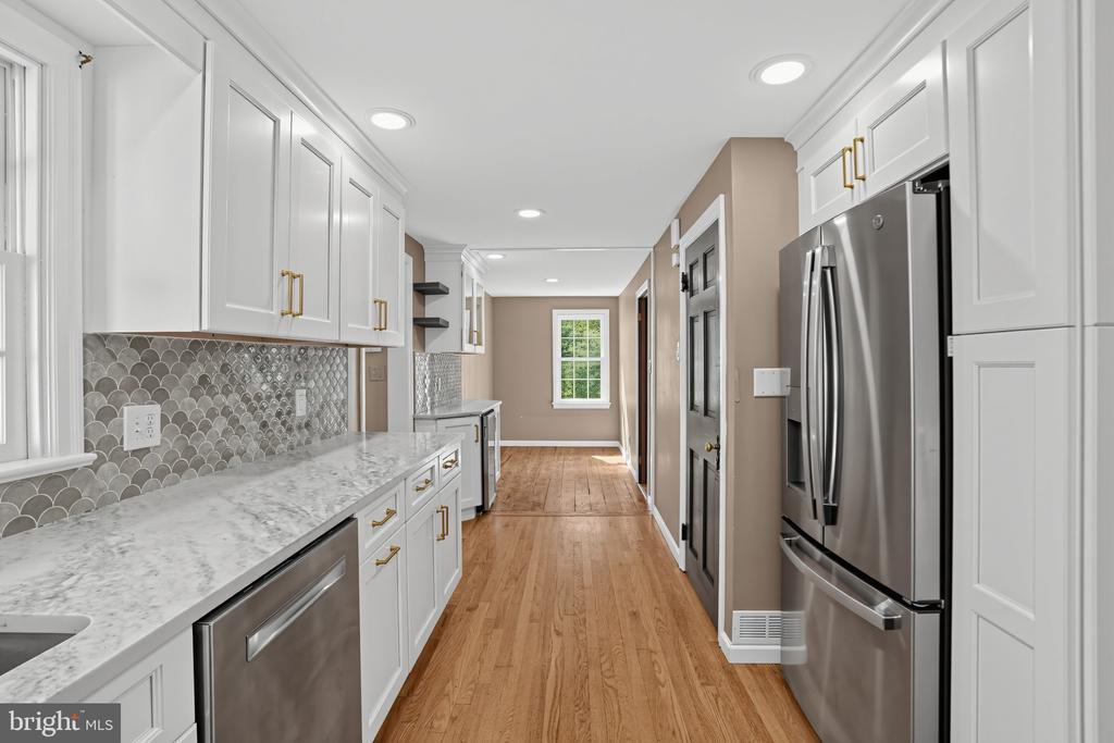 Kitchen with white cabinetry, scallop-pattern backsplash, marble-look counters, stainless appliances, and wood floors.