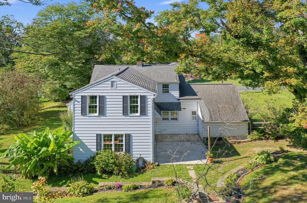 White-sided home with an attached garage, driveway, and landscaped yard beneath mature trees.