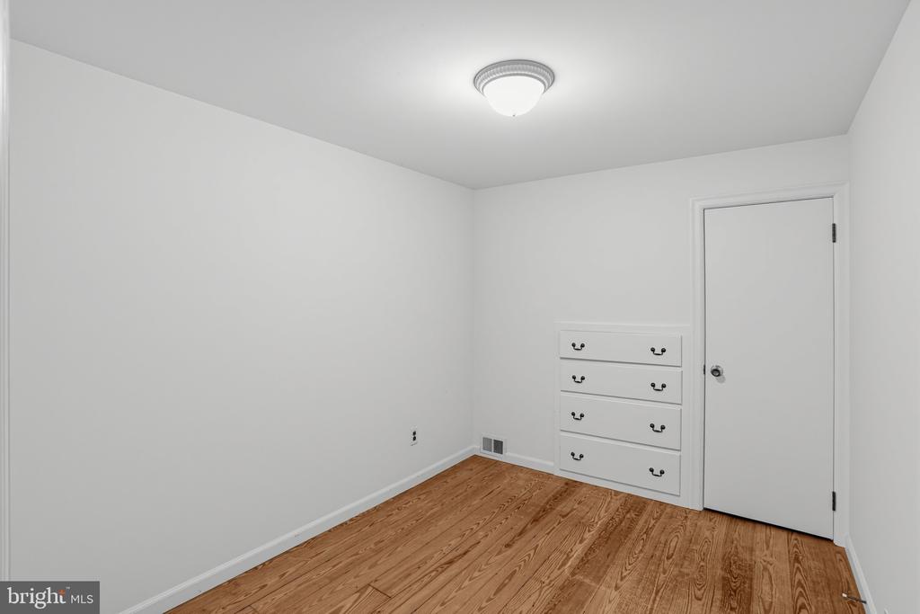 Empty bedroom with hardwood floors and a built-in dresser beside the door.