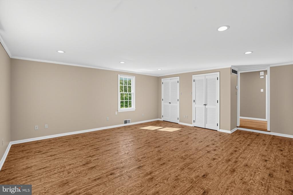 Empty room with warm wood flooring, white louvered closet doors, and a window overlooking greenery.