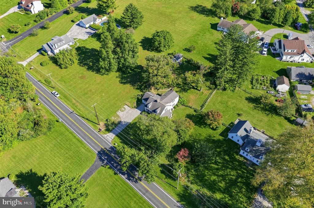 Aerial view of a home amid broad lawns and mature trees beside a two-lane road.