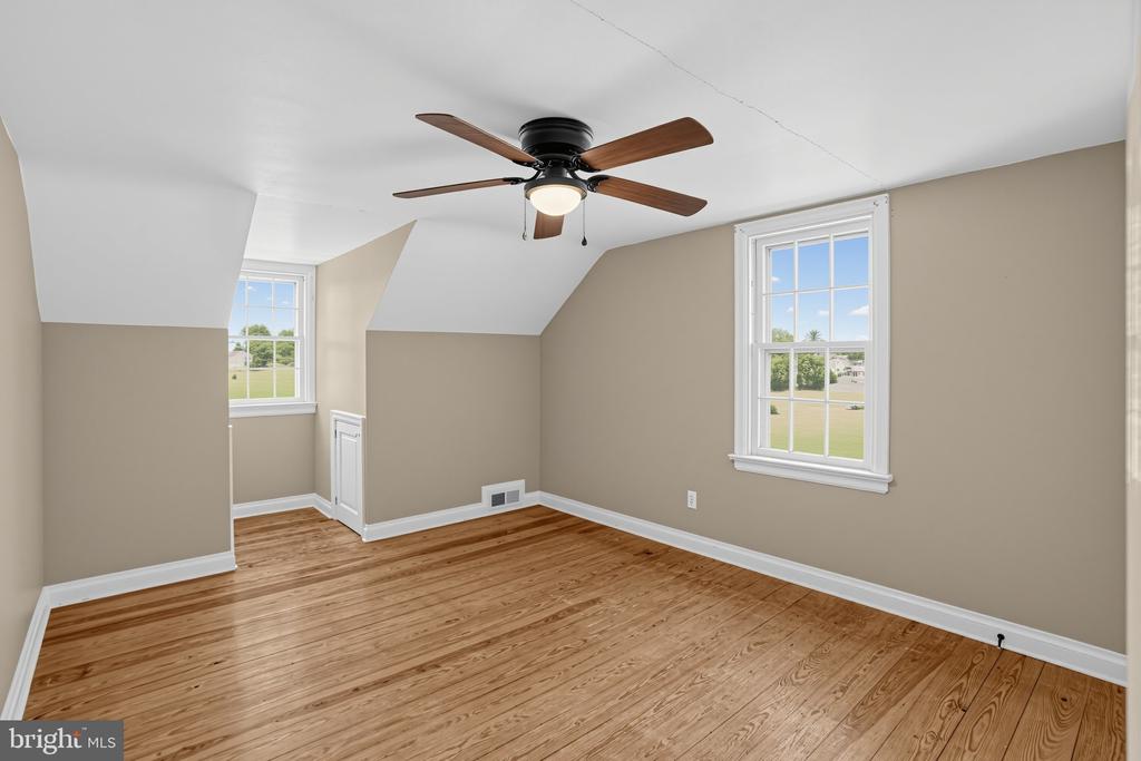 Empty bedroom with hardwood floors, two windows, and a ceiling fan beneath a sloped ceiling.