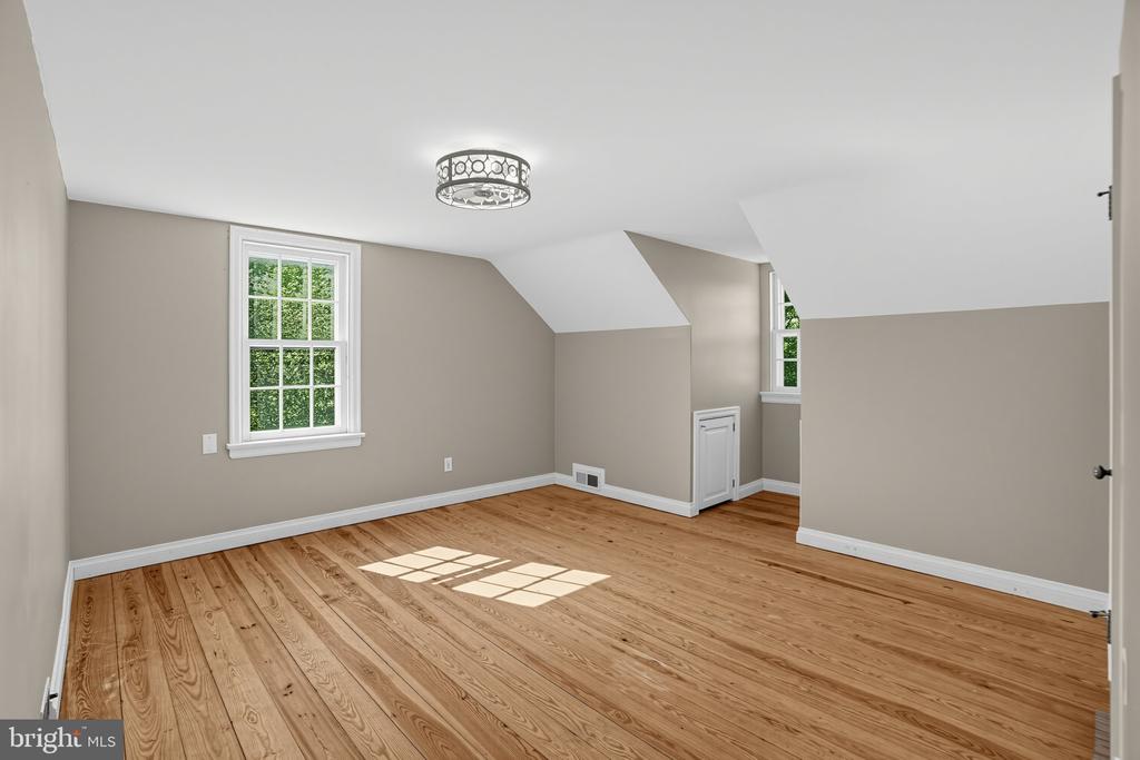 Vacant upstairs room with hardwood floors, sloped ceiling, and two windows.