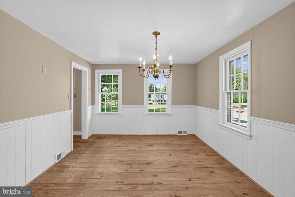 Vacant dining room with wide-plank wood floors, white wainscoting, and a brass chandelier.