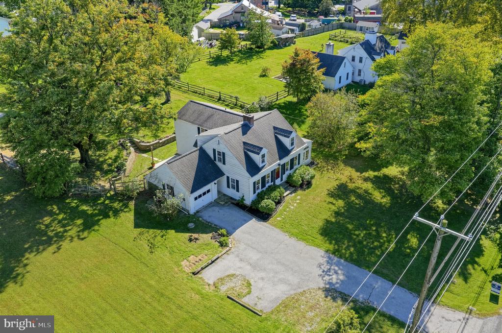 White two-story house with dark gabled roofs, broad lawn, and mature trees, seen from above.