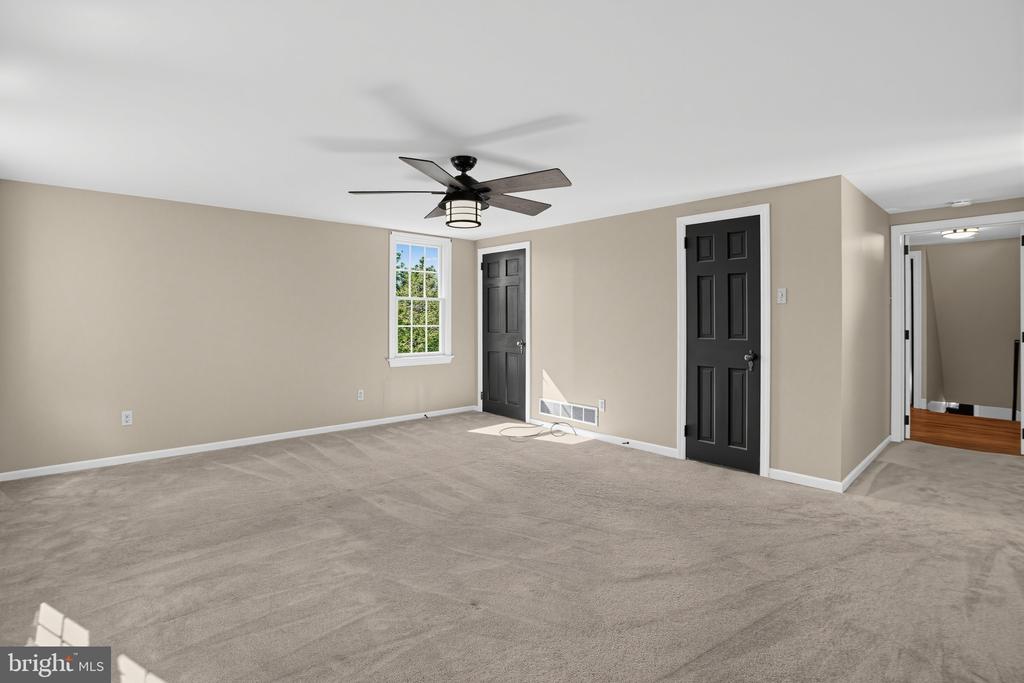 Empty carpeted room with a ceiling fan, one window, and two black doors.