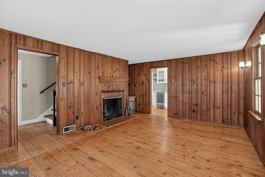 Empty wood-paneled living room with hardwood floors, a brick-surround fireplace, and tall windows.