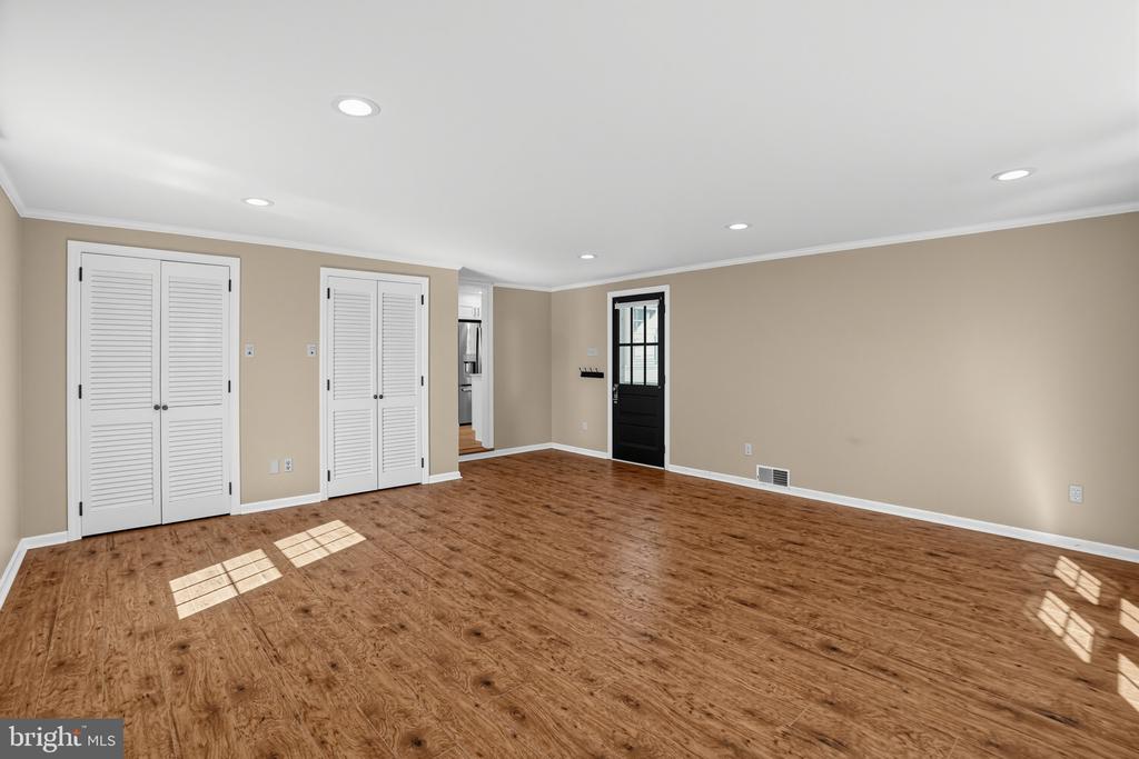 Vacant living room with wood floors, louvered closet doors, and a black exterior door.