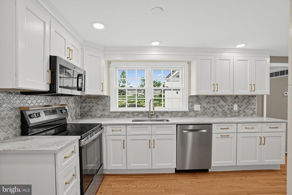 Kitchen with white cabinets, gray scalloped backsplash, stainless steel appliances, and a window over the sink.