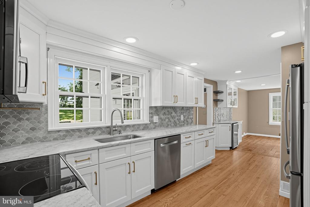 Kitchen with white cabinetry, gray scallop-tile backsplash, stainless steel appliances, and hardwood floors.