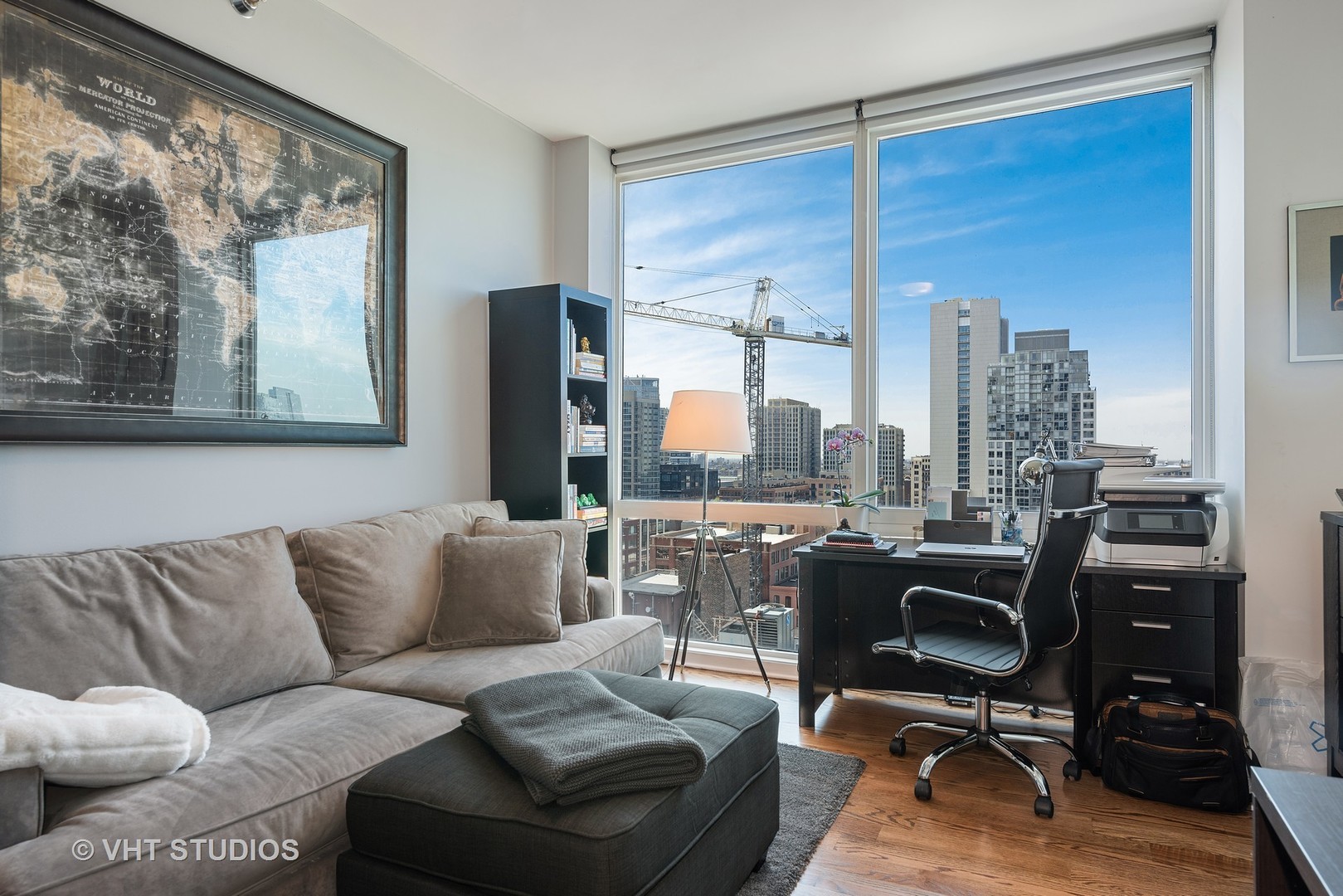 Furnished condo living room and office with floor-to-ceiling windows overlooking downtown buildings.