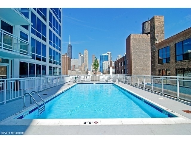 Rooftop swimming pool with city skyline beyond glass railings.
