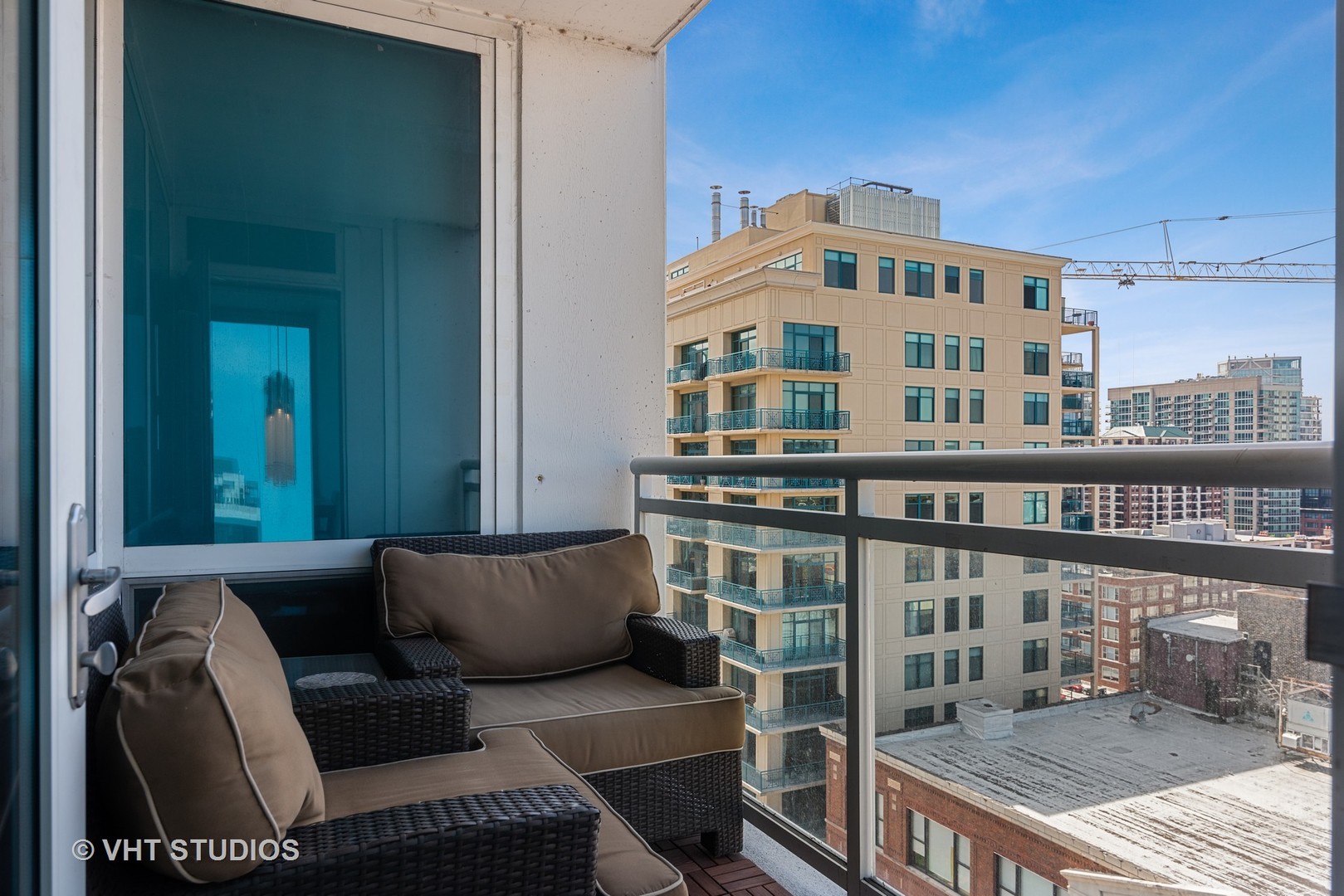 Furnished condo balcony with wicker seating and views of nearby city buildings.