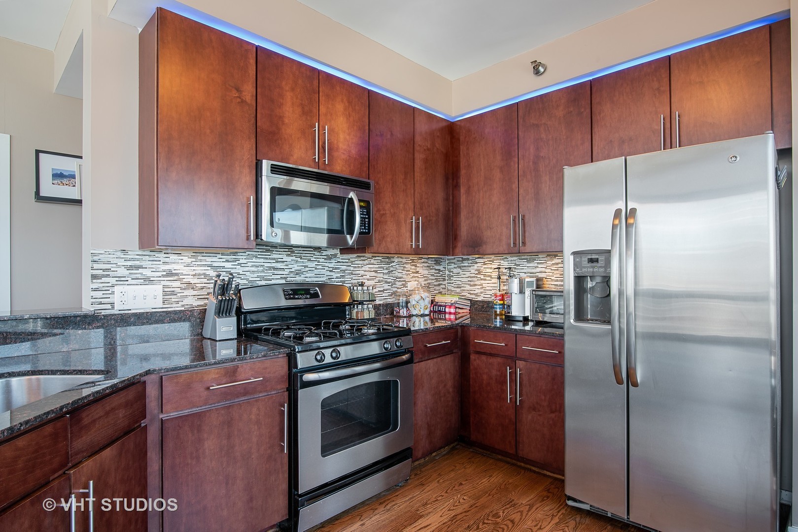 Kitchen with dark wood cabinets, granite counters, mosaic backsplash, and stainless steel appliances.
