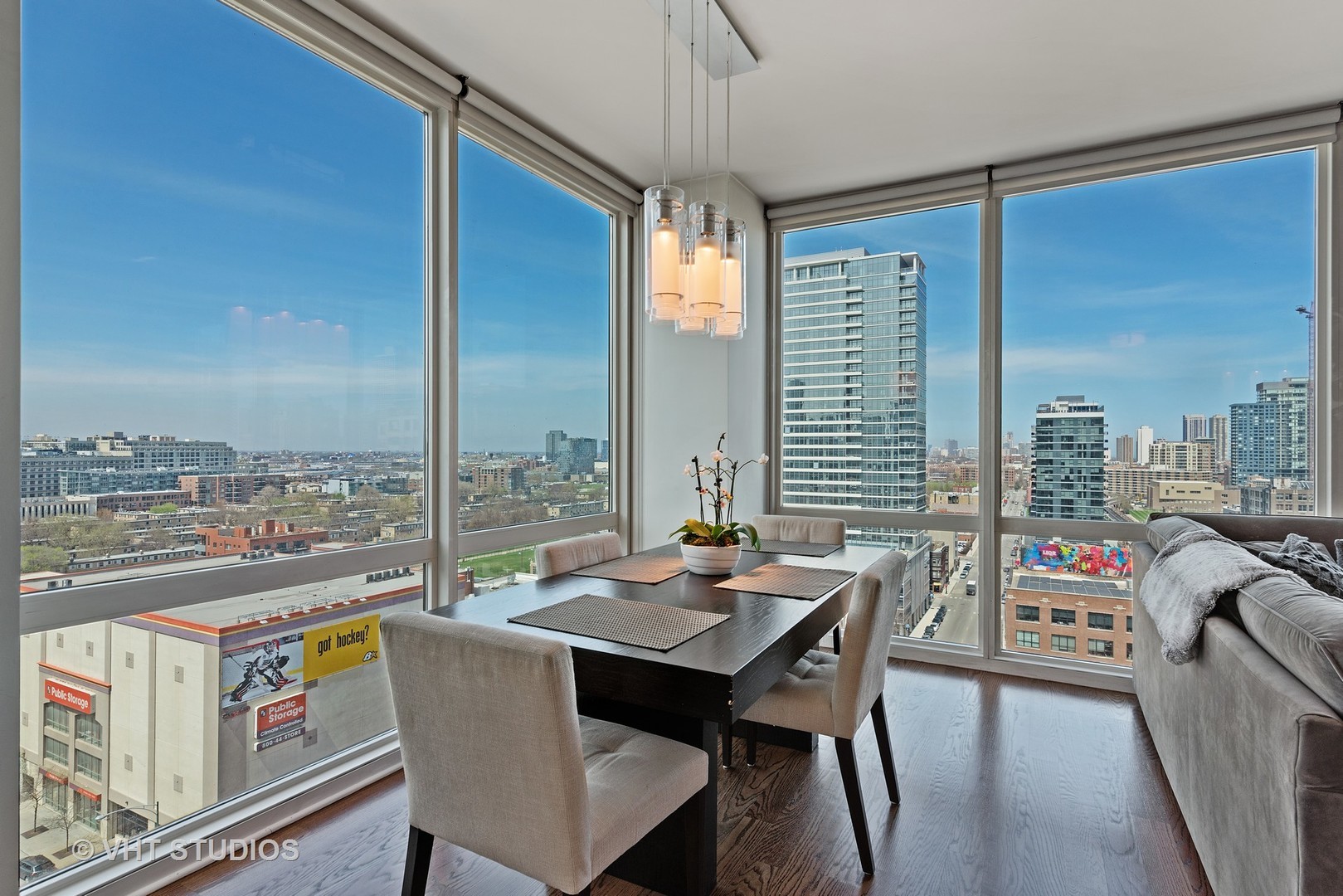 Dining area with floor-to-ceiling corner windows overlooking the city and a dark wood table.