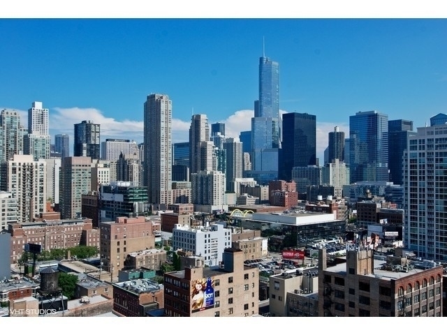 Downtown Chicago skyline rising above lower rooftops under a clear blue sky.
