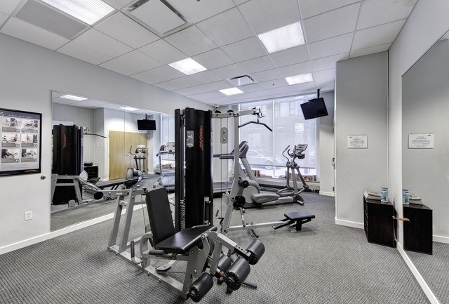 Condominium gym with weight machines and exercise bikes in front of large windows.