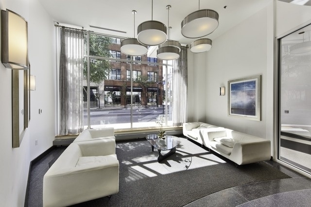 Furnished living room with white sofas, modern pendant lights, and floor-to-ceiling windows overlooking a city street.