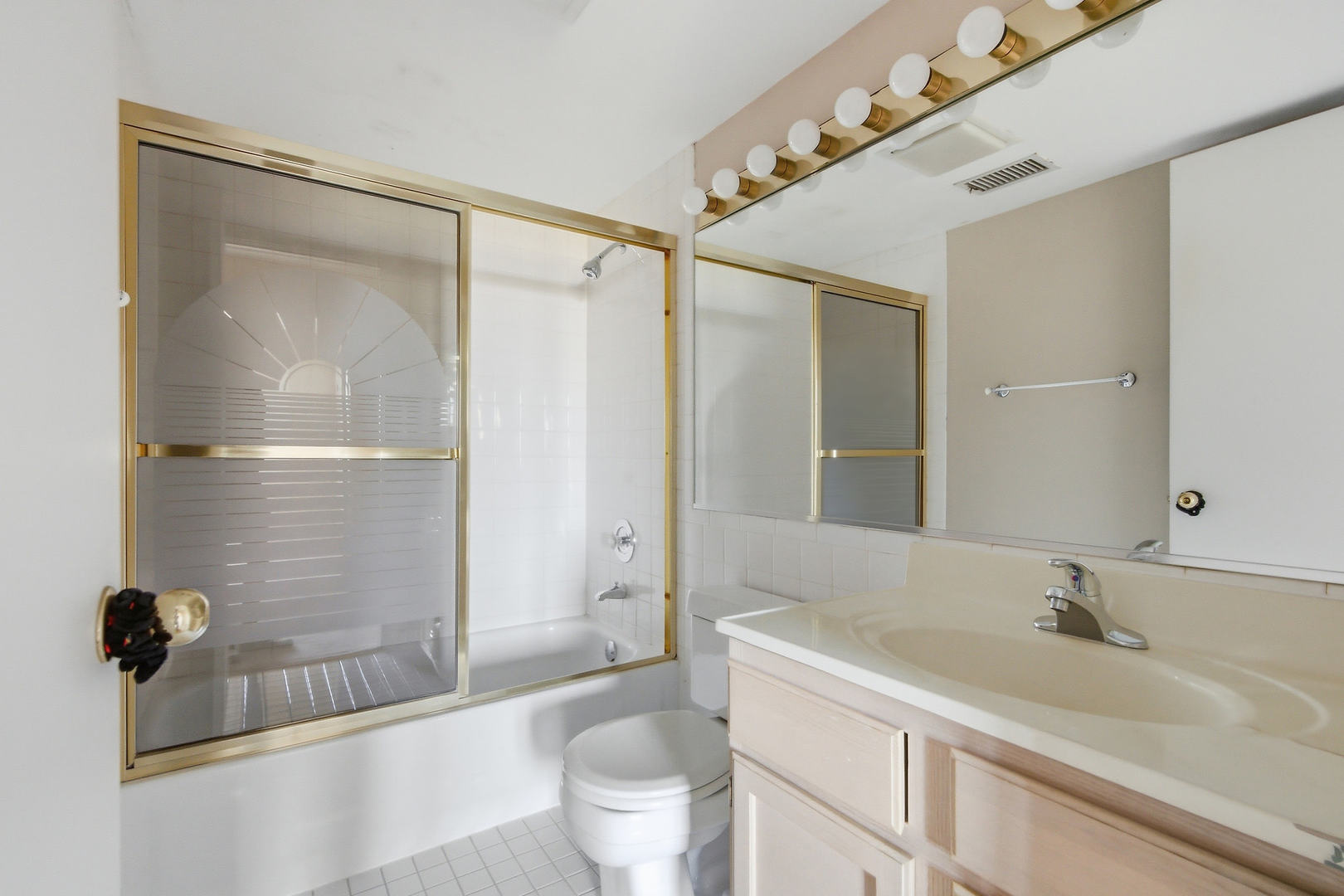 Bathroom with gold-trimmed shower doors, a mirrored wall, and a pale wood vanity.