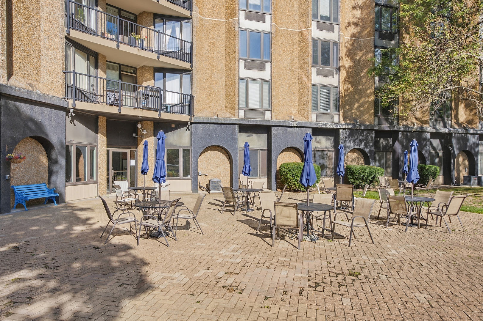 Residential courtyard with café seating, blue umbrellas, and balconies above.