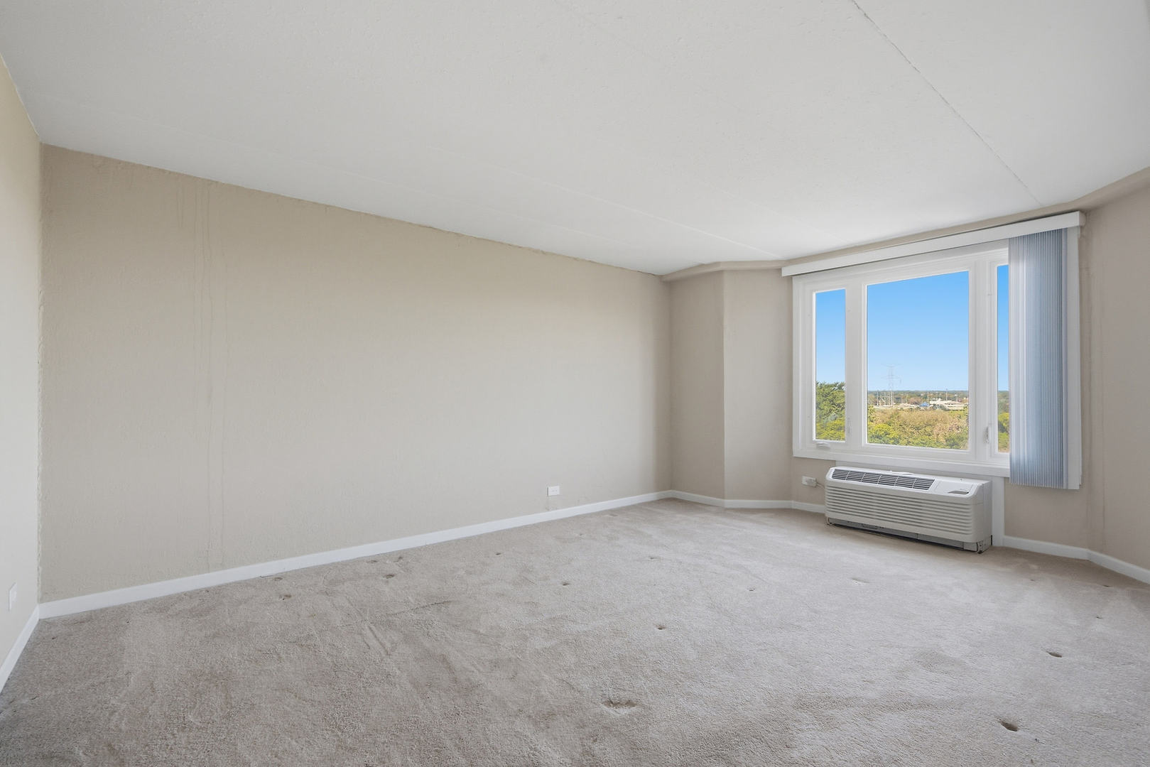 Vacant carpeted room with a large window and a through-wall air conditioner.