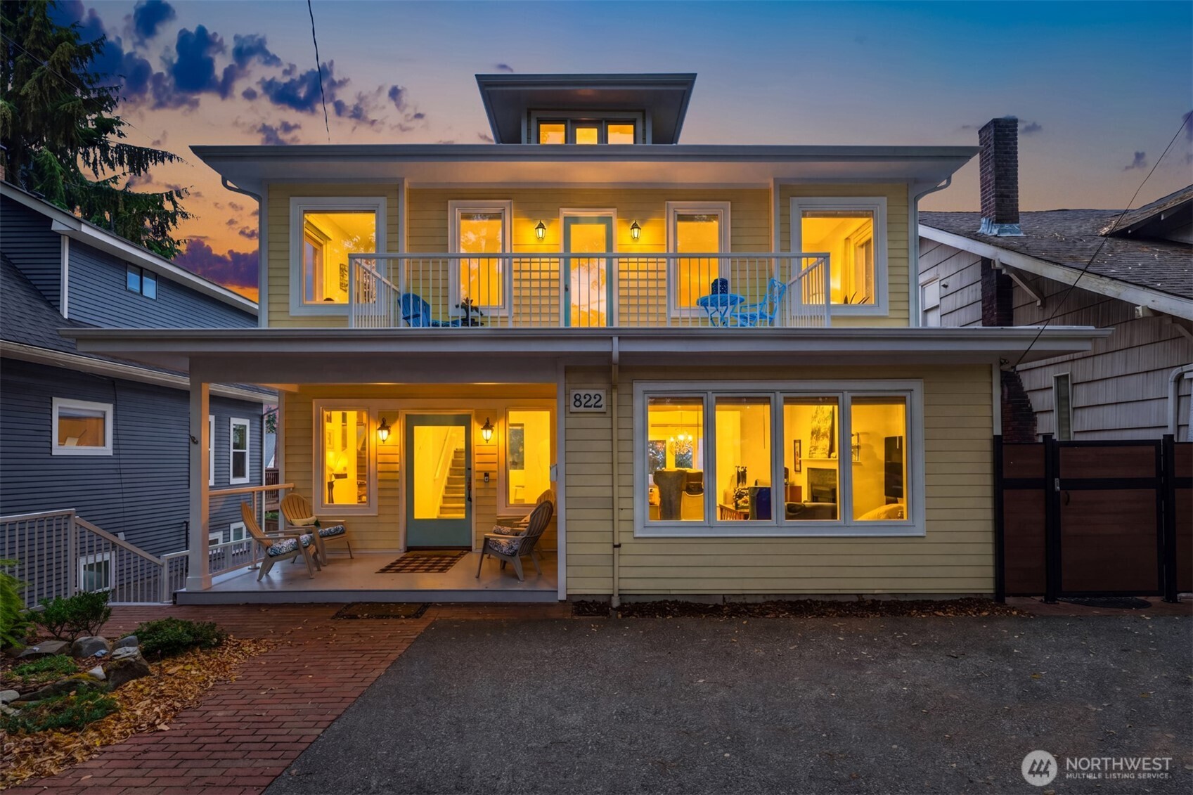 Two-story home with a covered entry porch and upper balcony glowing at dusk.