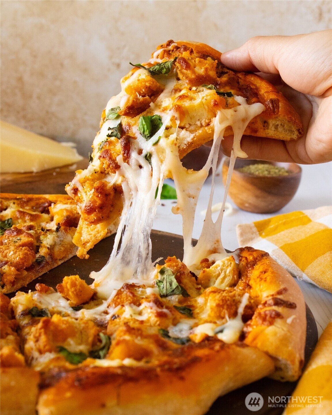 A hand lifts a slice of pizza with stretchy melted cheese and basil.