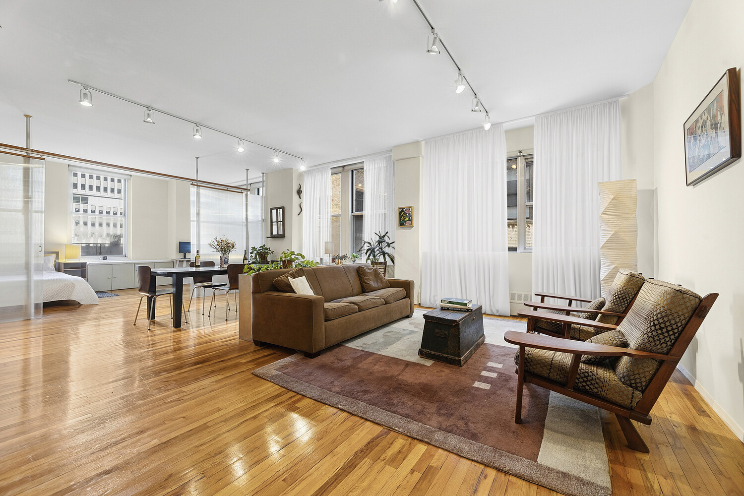 Open-plan loft living and dining area with hardwood floors, tall curtained windows, and brown seating.