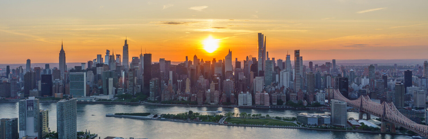New York City skyline at sunset, with the East River and Queensboro Bridge in the foreground.