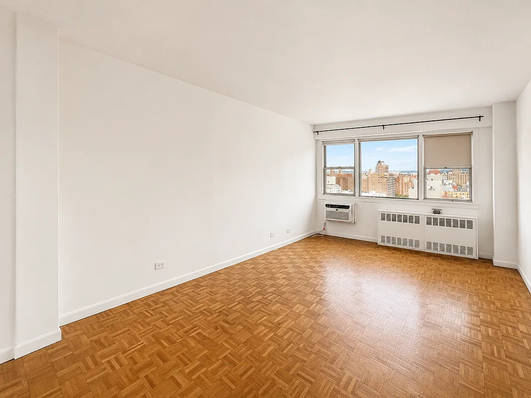 Empty apartment room with parquet floors and wide windows overlooking the city.