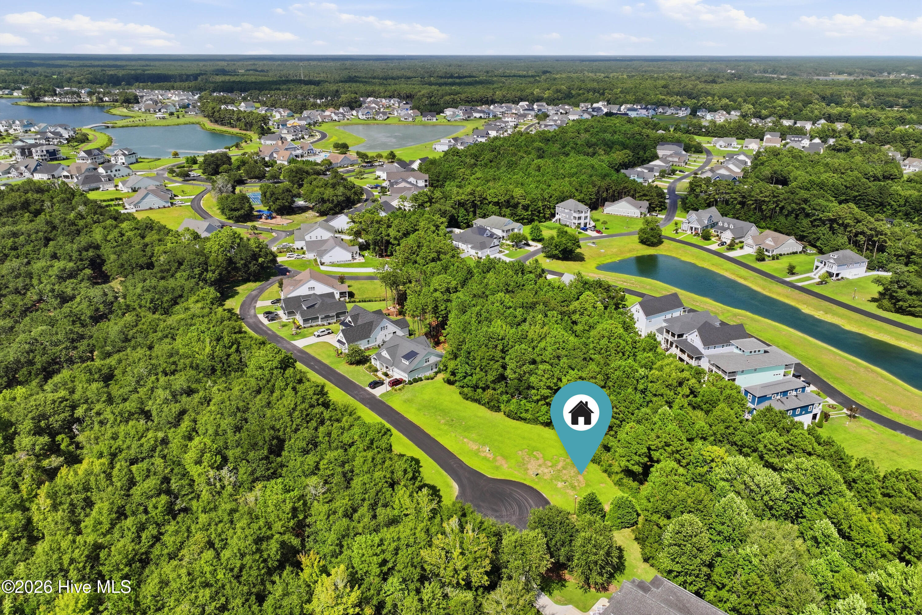 Aerial view of a wooded neighborhood with ponds and a marker identifying the property.