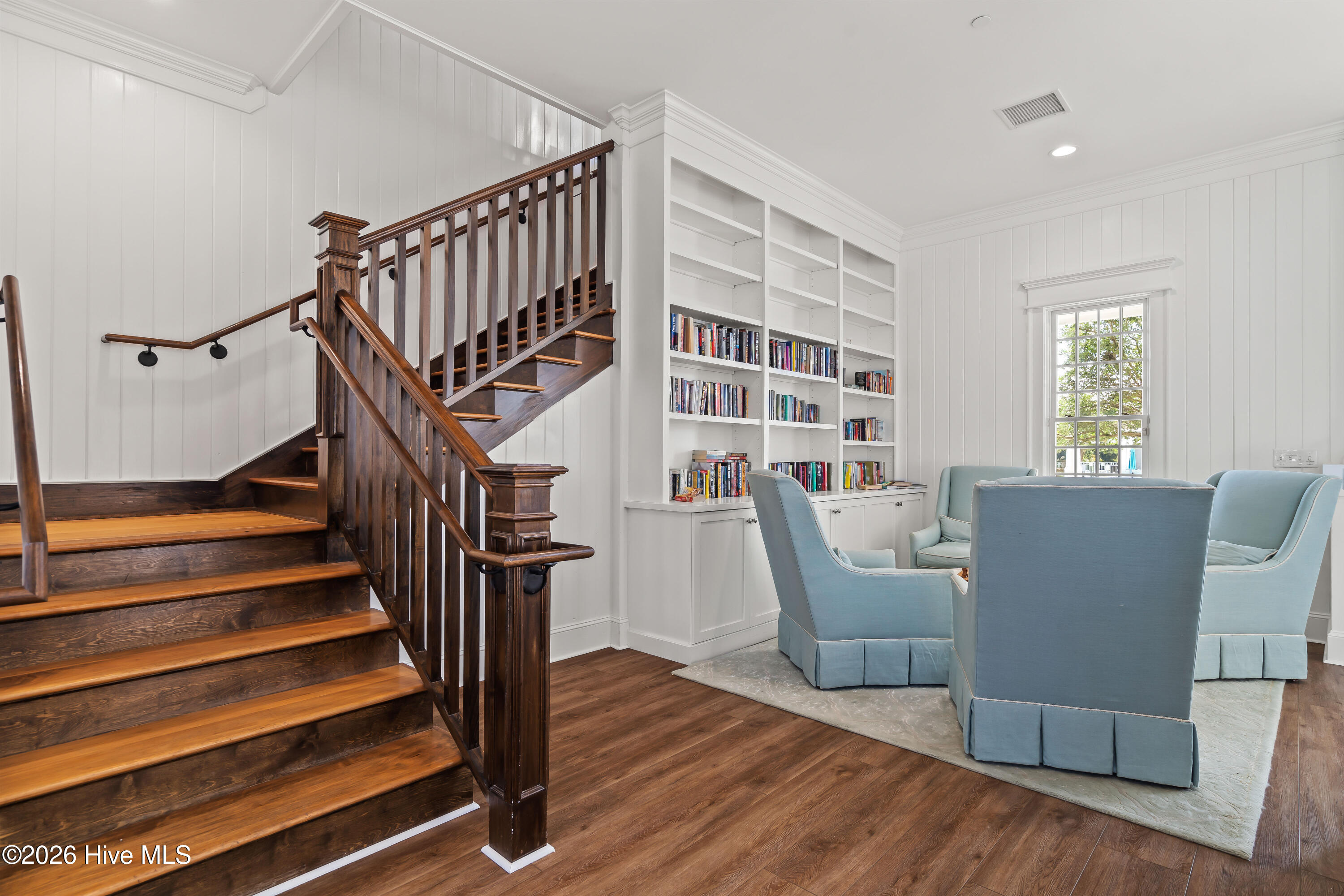 Living room with a dark wood staircase, built-in bookcases, and blue upholstered chairs.