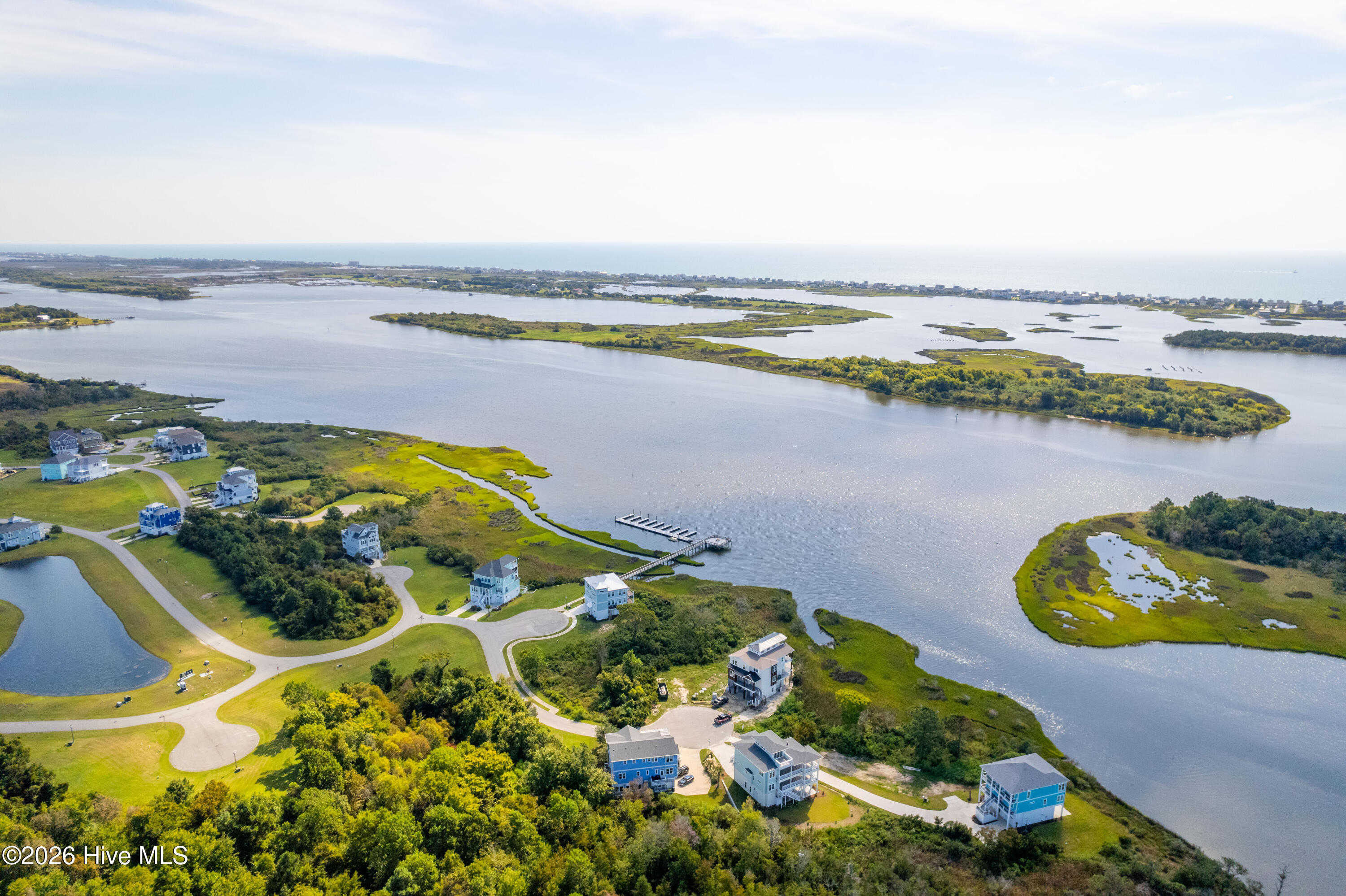 Aerial view of coastal homes beside a marsh-lined inlet, with a community dock and ocean horizon.