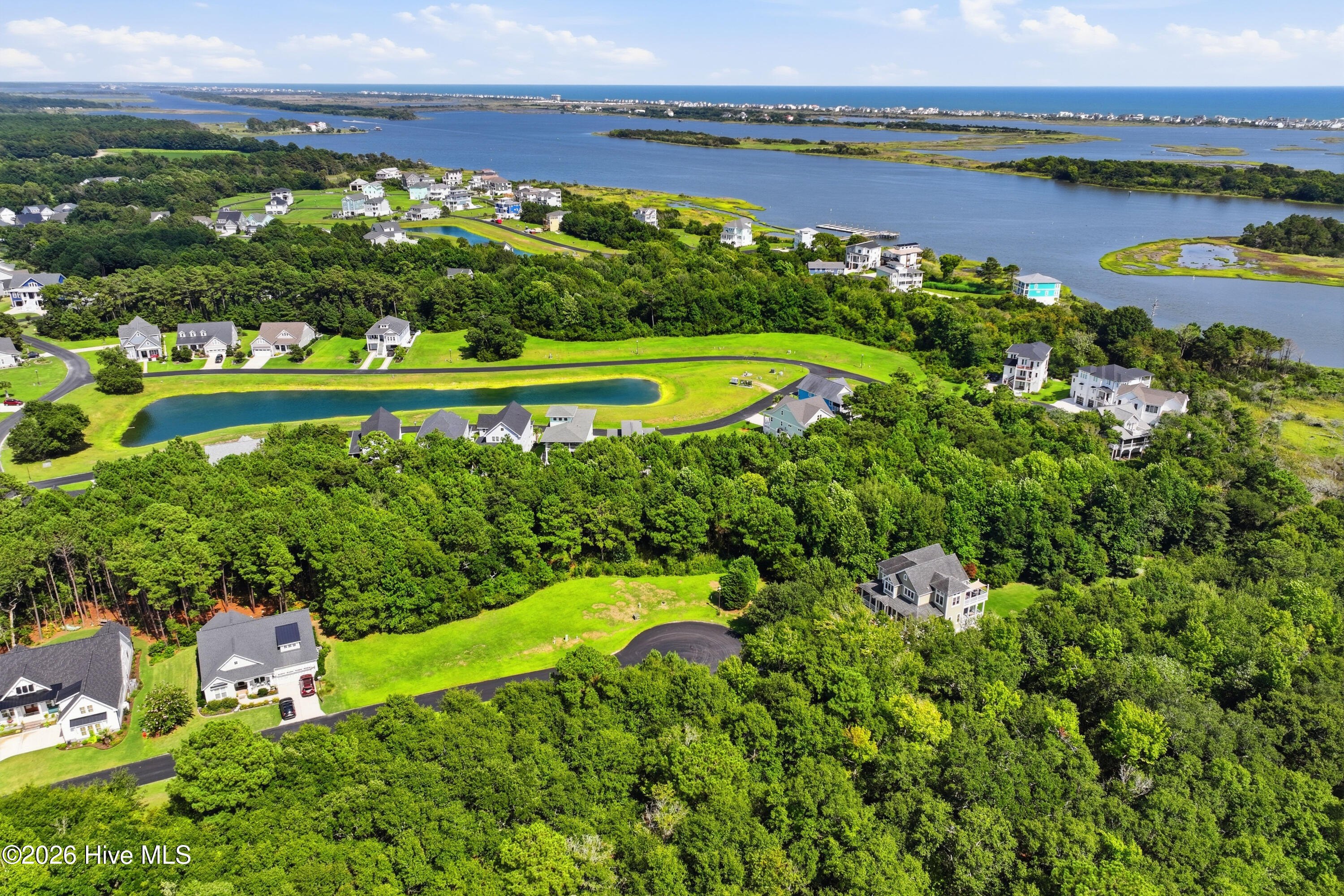 Aerial neighborhood beside coastal waterways, with wooded lots, homes, and a long pond.